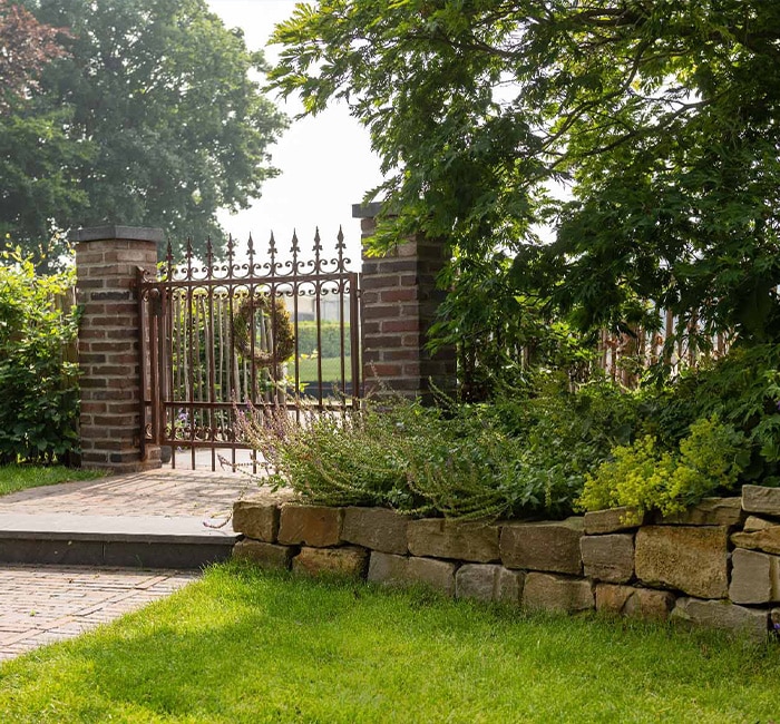 Eingangstor mit Gartenlandschaft Eingangstor aus Metall mit Ziegelmauer und Gartenpflanzen im Vordergrund.