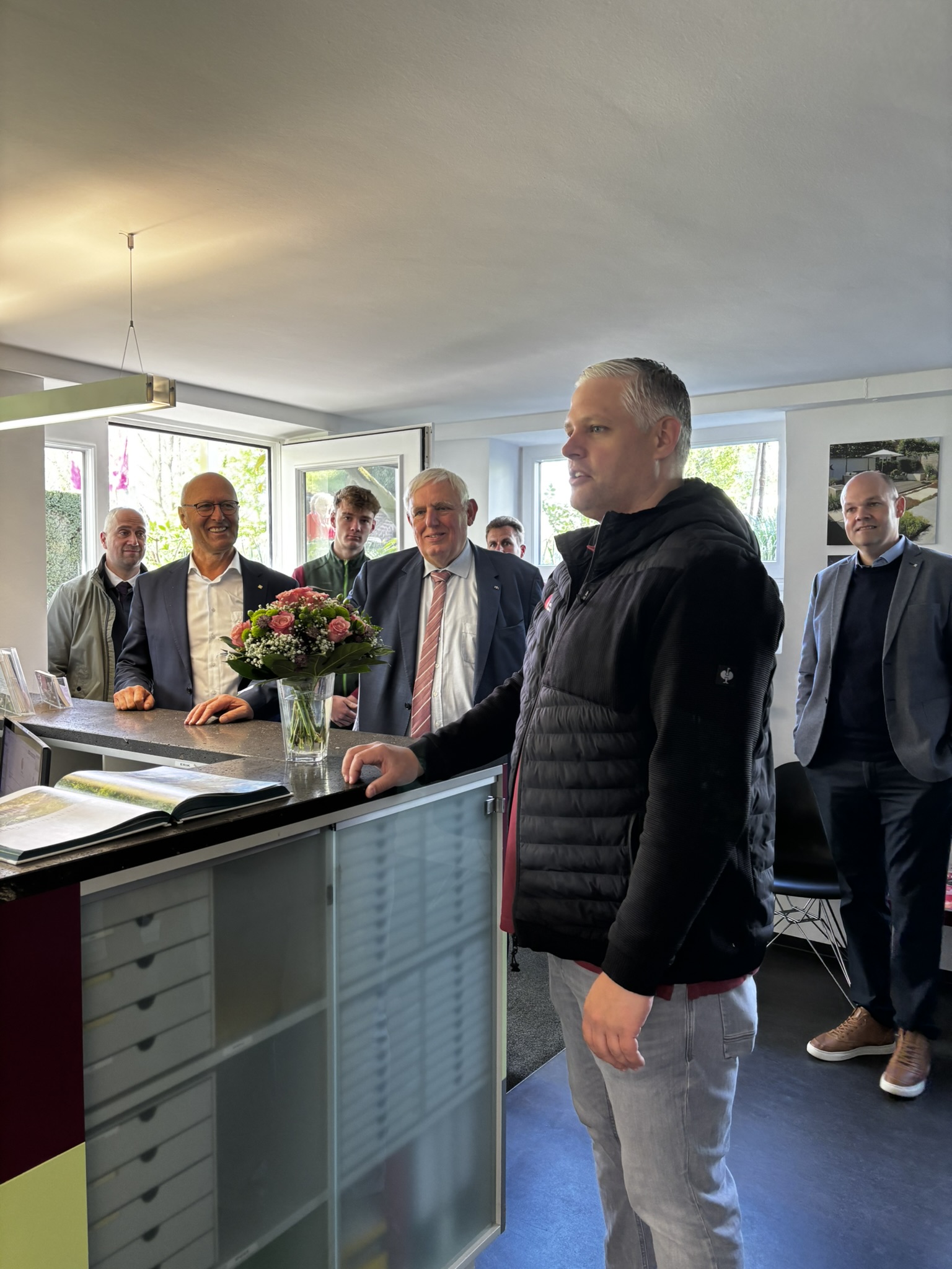 Bei einer Veranstaltung mit dem NRW-Minister-Ausbildungspreis stehen mehrere Personen im Anzug; im Vordergrund ein Blumenstrauß und ein blaues Sakko.