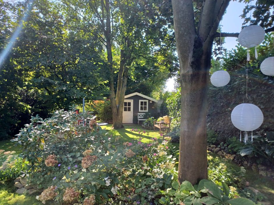 Eine Statue einer sitzenden Figur mit einer Krone in einem Garten mit Blumen und Pflanzen.