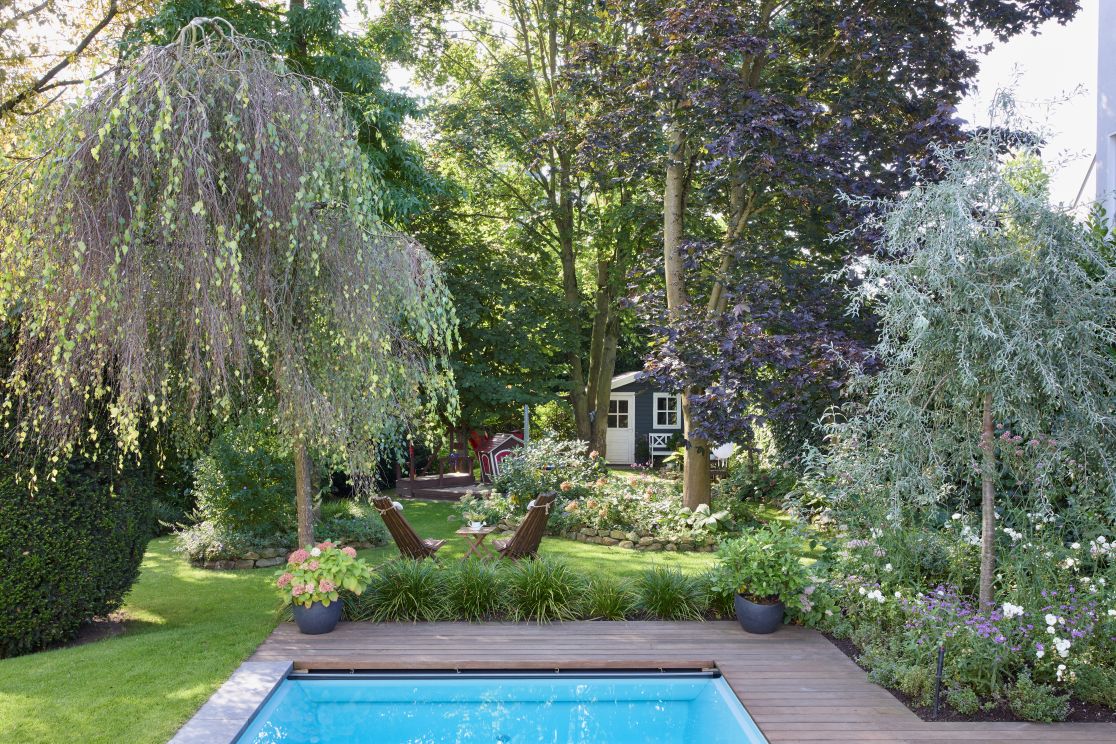 Ein modernes Holzhaus mit großen Fenstern in einem Garten mit bunten Blumen und Rasen.