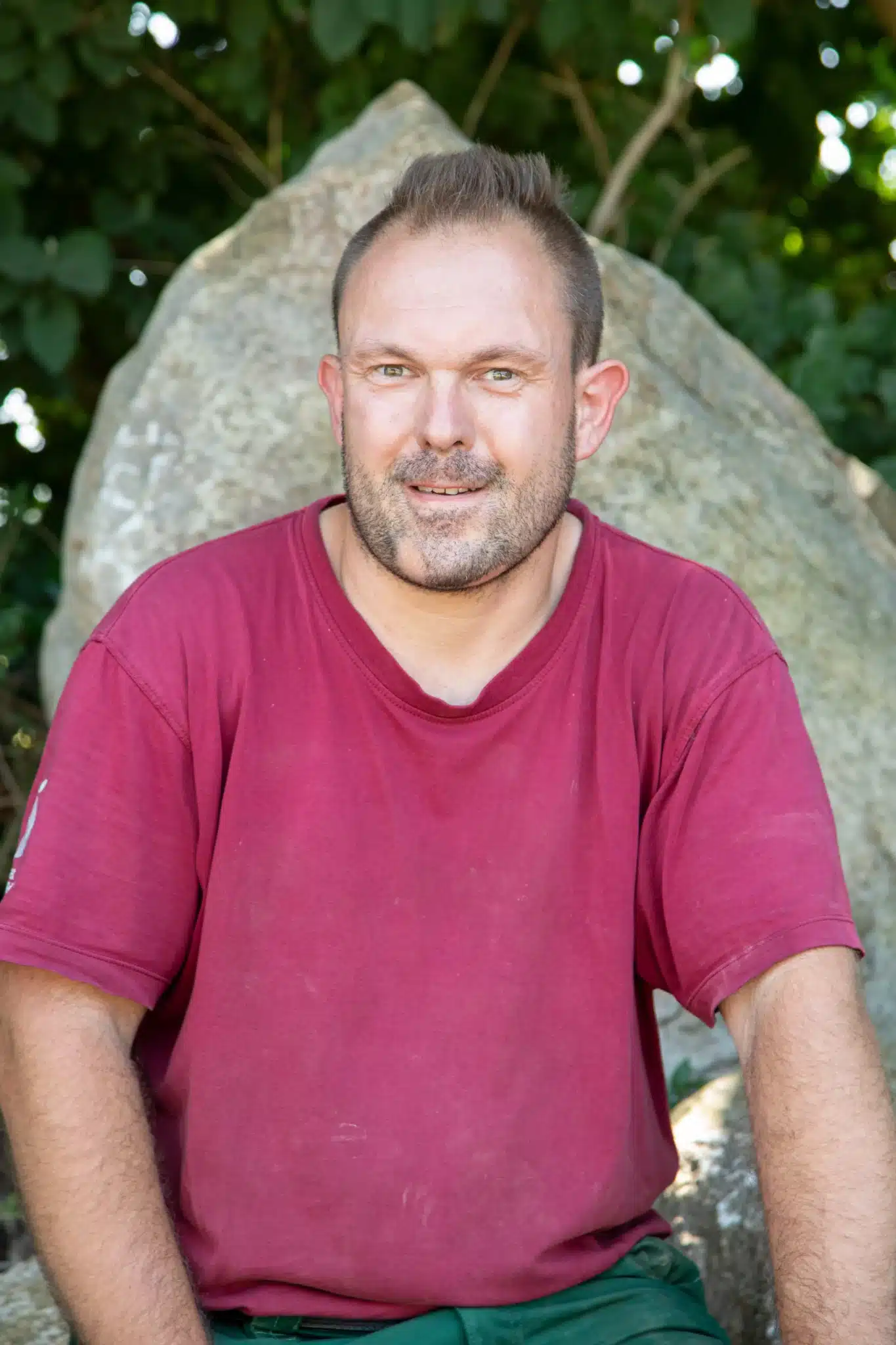 Porträt eines Mannes mit kurzem Haar, der ein rotes T-Shirt trägt und in die Kamera lächelt.