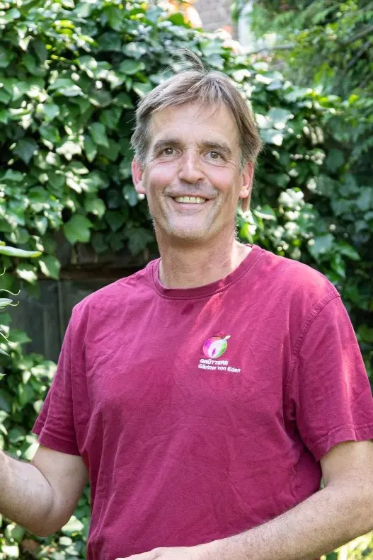 Ein Mann mit braunem T-Shirt und mittellangen Haaren, der in die Kamera lächelt.