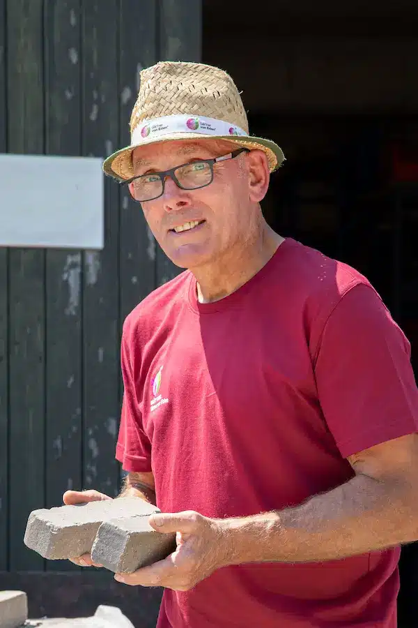 Mann mit Brille und grüner Kappe, der in die Kamera lächelt, trägt ein rotes T-Shirt.