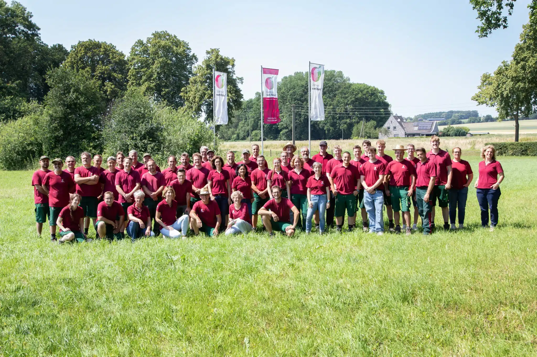 Gruppenfoto von Mitarbeitern, die rote Shirts und grüne Hosen tragen, auf einer Wiese.