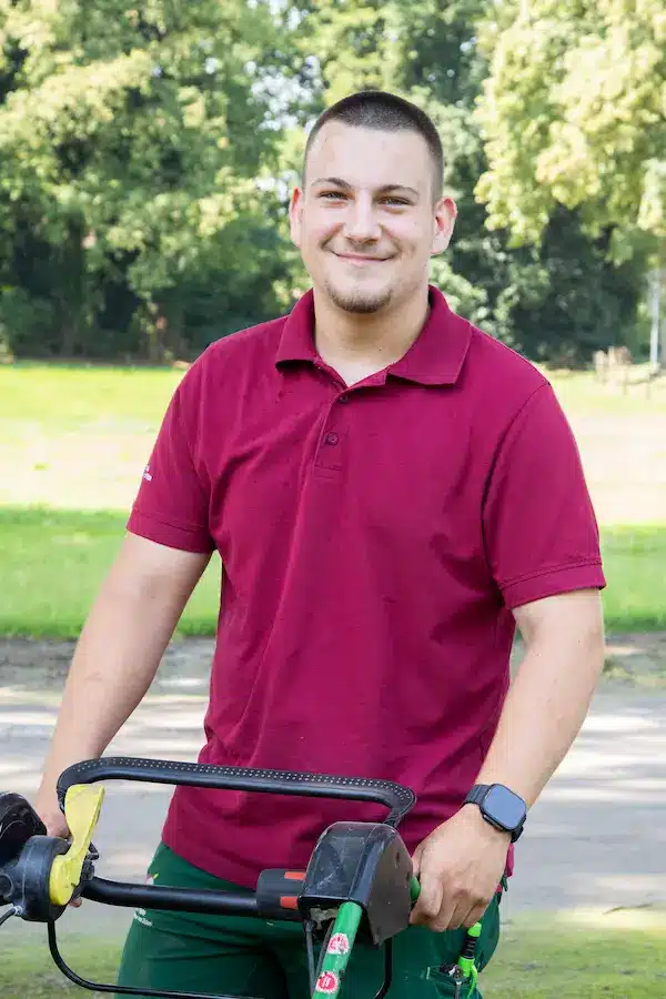 Junger Mann mit nassem rotem T-Shirt steht vor einer Holzoberfläche.