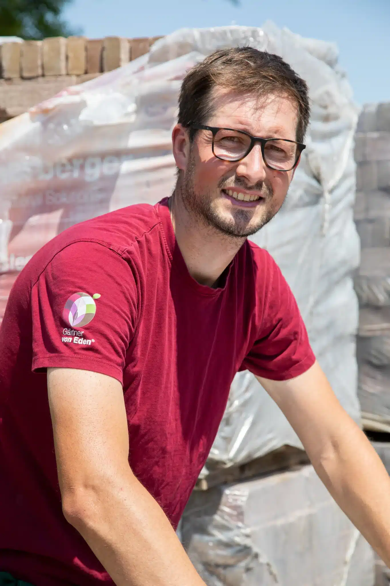 Mann mit Brille und rotem Poloshirt lächelt in die Kamera.