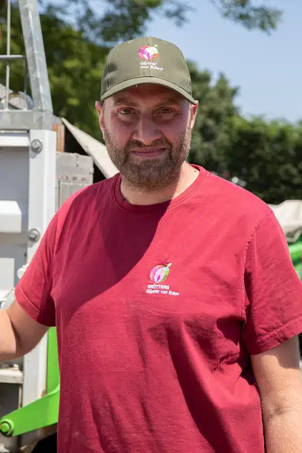 Mann mit Bart trägt eine grüne Weste und eine schwarze Kappe mit dem Schriftzug 'ES'.
