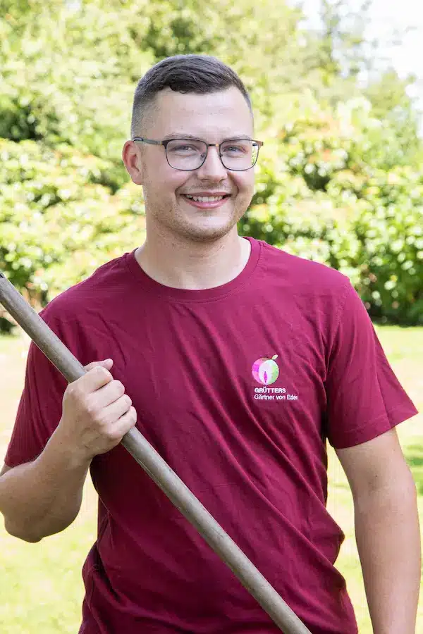 Junger Mann mit Brille, der ein rotes T-Shirt trägt und vor einem grünen Hintergrund steht.