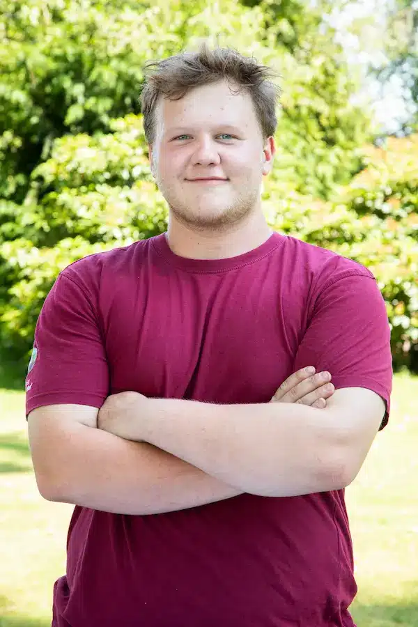Junger Mann mit blonden Haaren und Brille, der in die Kamera schaut.