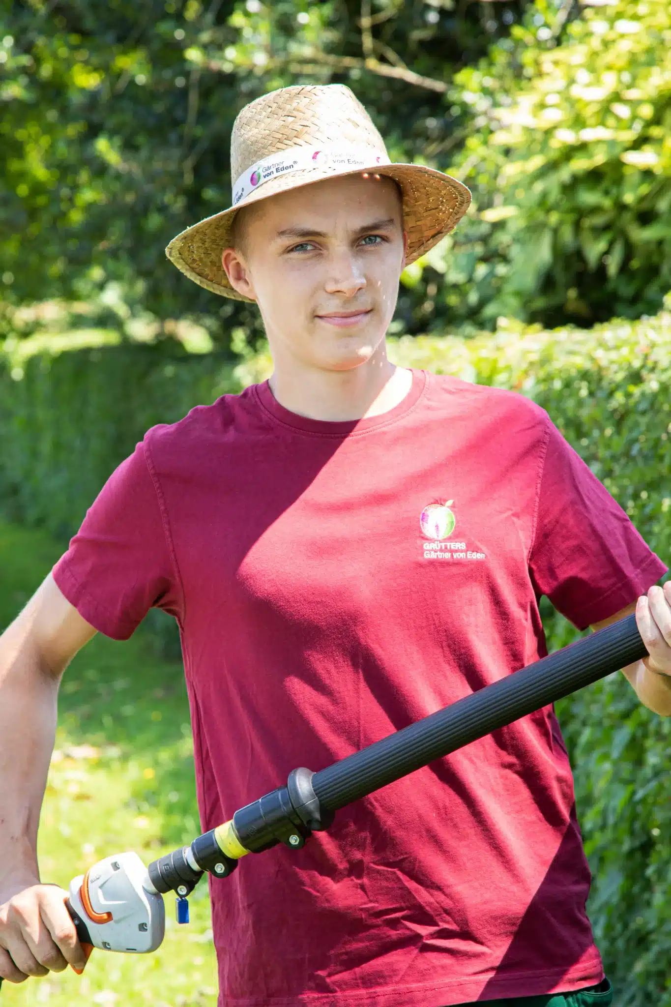 Ein Mann mit Brille und Kappe lächelt in die Kamera, während er ein rotes T-Shirt trägt.