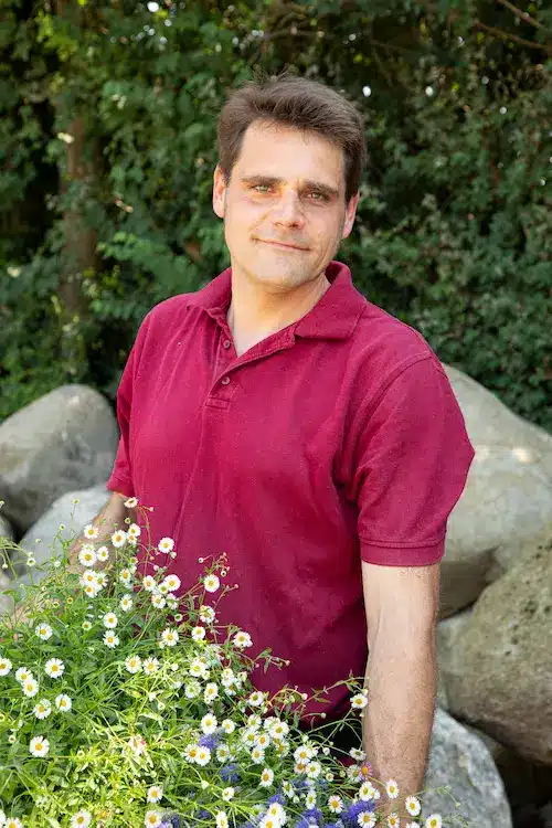 Mann mit kurzen Haaren und einem roten Poloshirt, der in die Kamera lächelt.