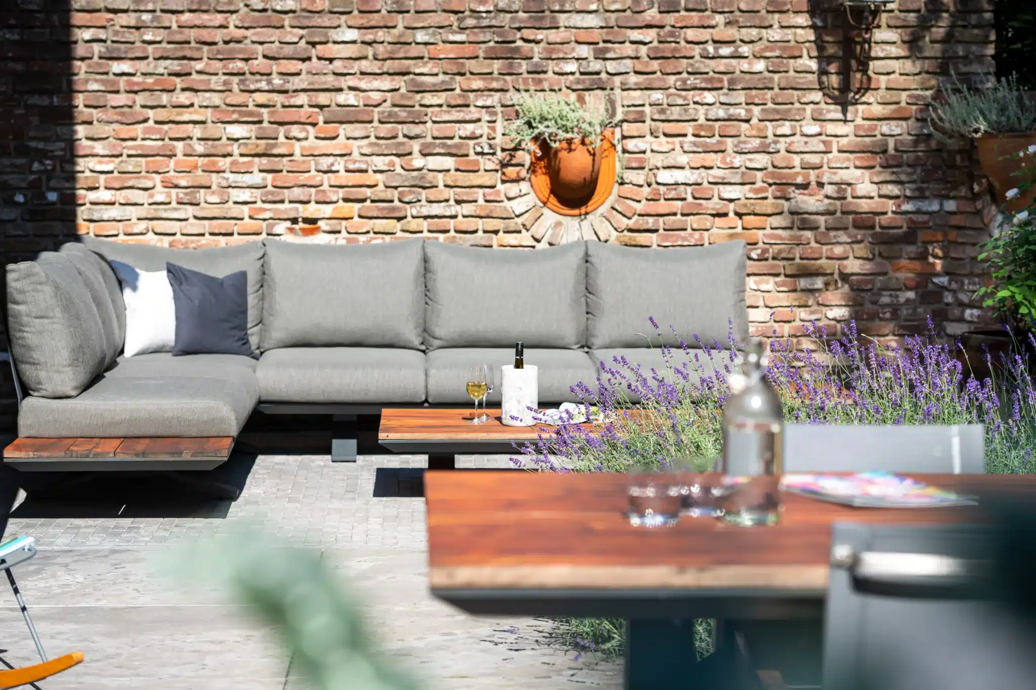 Terrasse mit Lounge und Lavendel Terrasse mit grauem Loungesofa vor einer rustikalen Backsteinmauer, Holztischen und blühendem Lavendel.
